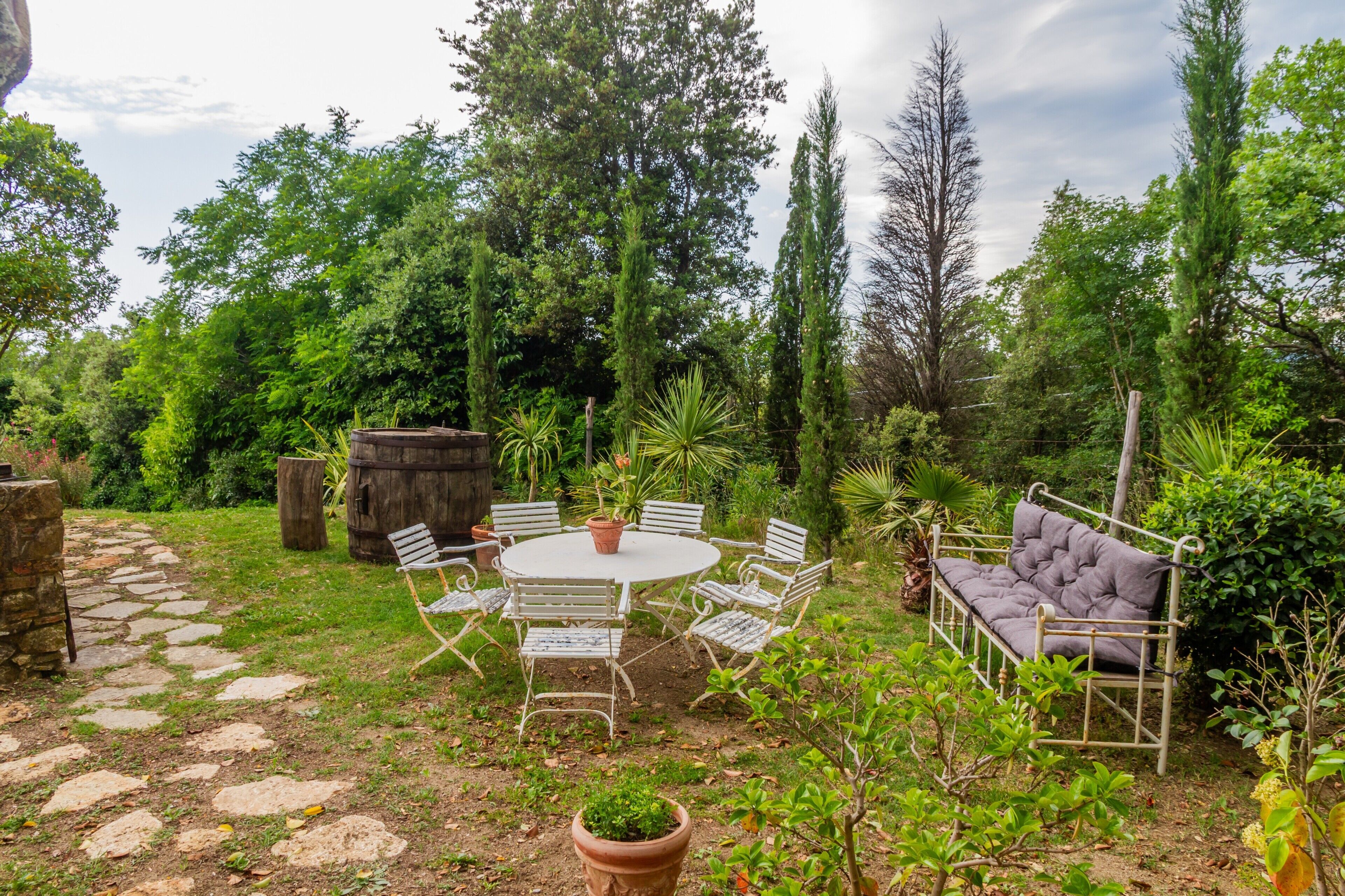 Une terrasse de jardin avec une table ronde, des chaises en métal blanc et un banc rembourré.