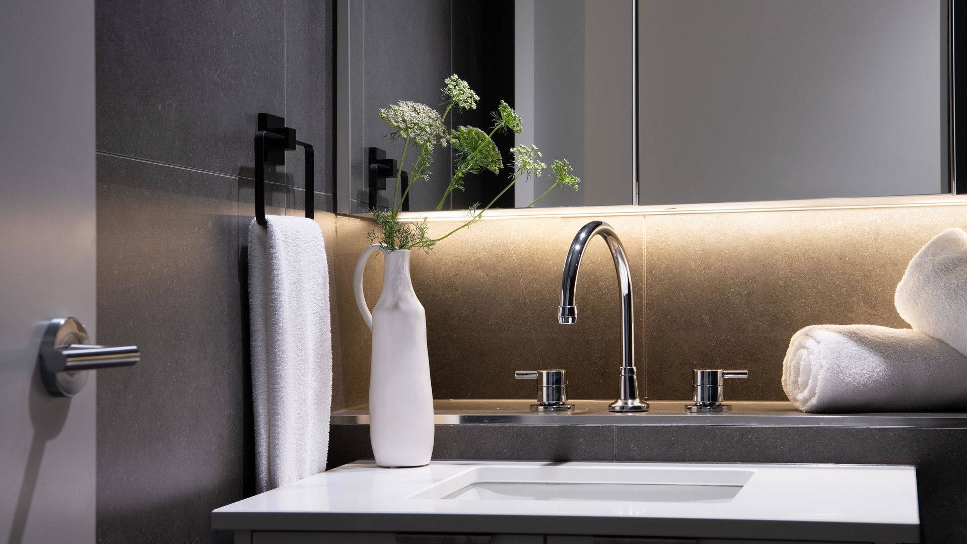 Un baño moderno con un lavamanos blanco, dos grifos y un perchero para toallas.