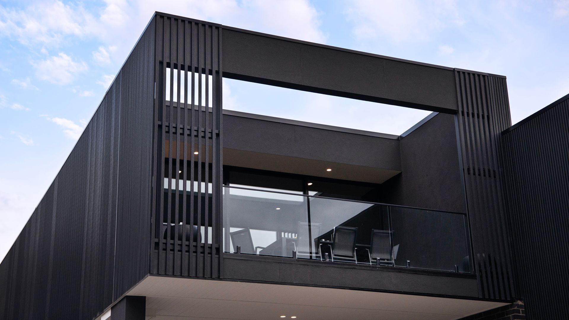 Ein modernes Gebäude mit Flachdach, großen Glasfenstern und einem Balkon mit Sitzgelegenheiten.