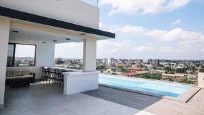 Une terrasse extérieure moderne dotée d’une piscine, d’un espace salon et offrant une vue sur le paysage urbain.
