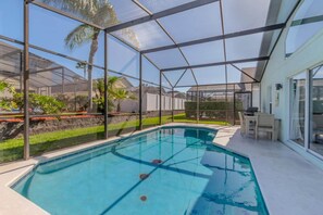 Ein Schwimmbecken mit Glasveranda, umgeben von einer Terrasse mit Gartenmöbeln.