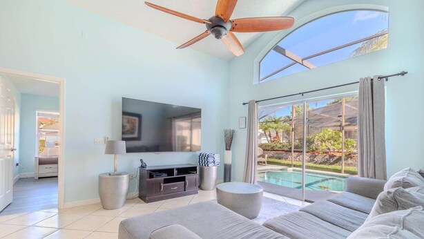 Un salon spacieux doté d’un ventilateur de plafond, d’un téléviseur à écran plat, d’un canapé confortable et offrant une vue sur une piscine grâce à de grandes portes-fenêtres coulissantes.