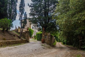 Ein Kiesweg führt zu einem Gebäude mit einem Steintor, umgeben von Bäumen und Grün.