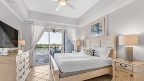 A bedroom with a bed, bedside tables, a ceiling fan, a window with curtains, and a view of the outdoors. - The Wharf 321 🌴 Luxury 2BR Condo w/ Marina Views + Balcony Grill (Orange Beach)