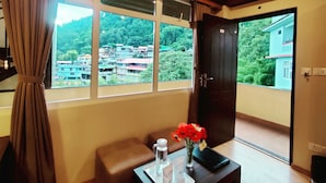A room with a large window, a door, a small table with a vase of flowers, and a water bottle. - Keswani Group Tashi Heritage Hotel (Gangtok)