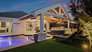 Ein modernes Haus mit Schwimmbad, Sitzgelegenheiten im Freien und einer überdachten Terrasse.