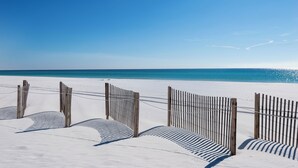 Een zandstrand met houten omheiningen en een helderblauwe lucht.