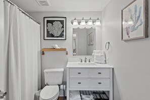 Une salle de bain moderne avec des toilettes blanches, un lavabo surmonté d’un miroir et un rideau de douche.