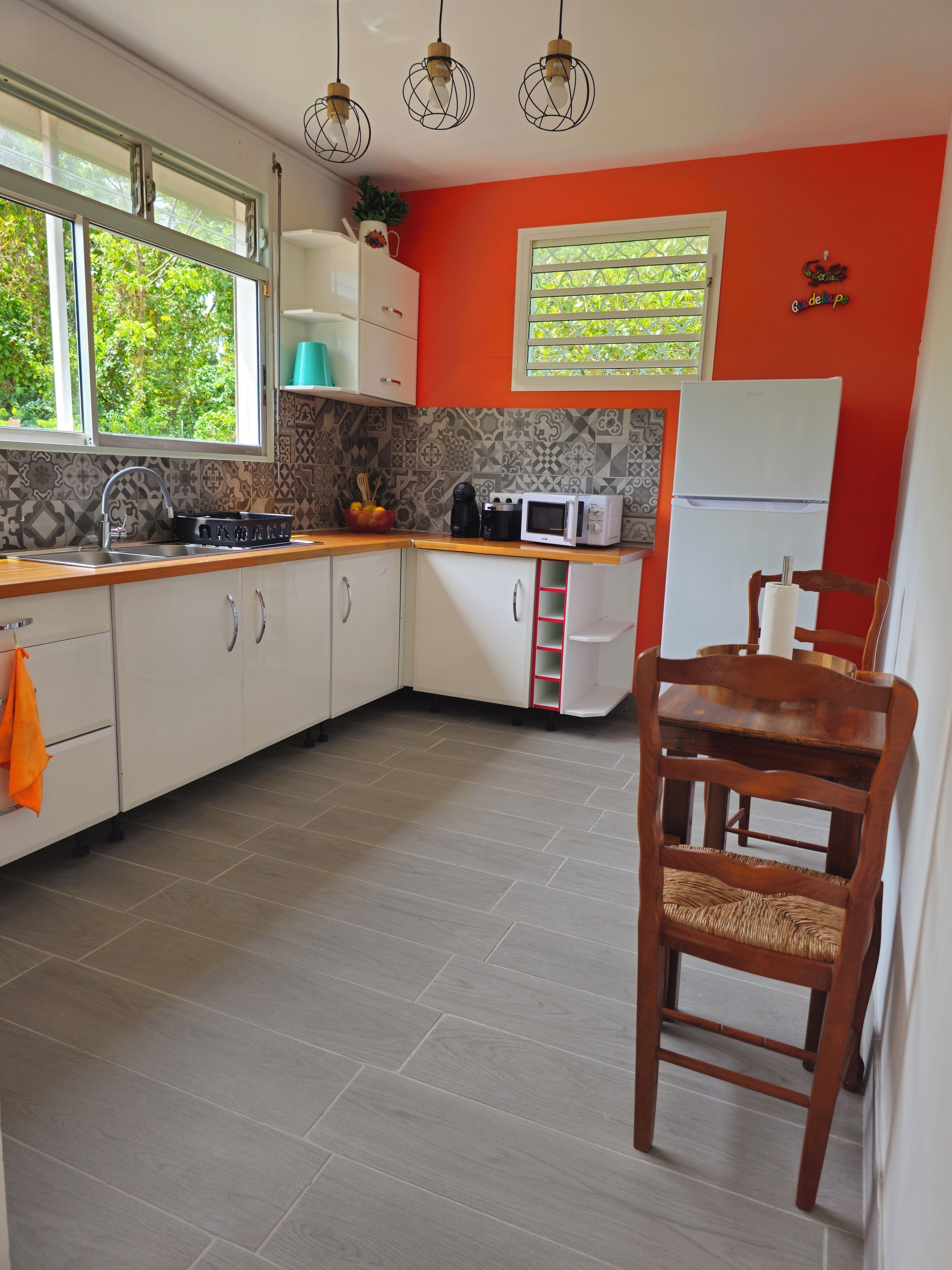 Uma cozinha moderna com armários brancos, bancada de madeira, geladeira branca e um espaço de refeições com mesa e cadeira de madeira.