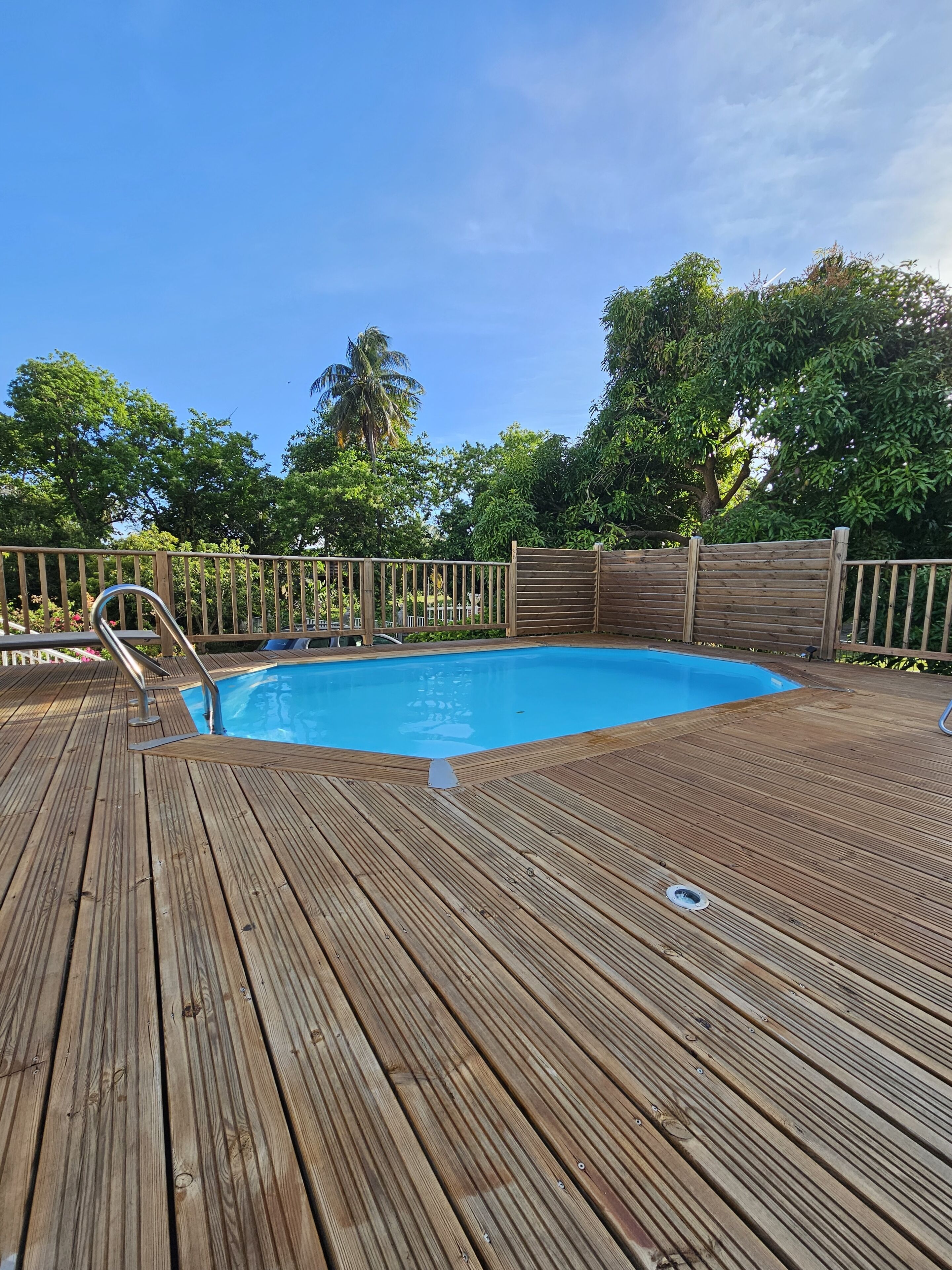 En træterrasse med swimmingpool, omgivet af et træhegn og træer.