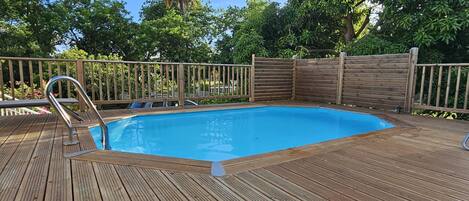 En træterrasse med swimmingpool, omgivet af et træhegn og træer.