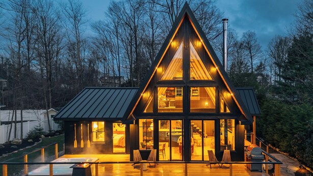 Una cabaña moderna con terraza de madera, ventanas amplias y techo de metal.