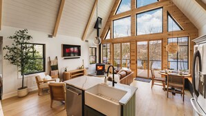 Amplia sala de estar con una chimenea grande, vigas de madera y vistas al exterior.