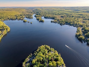 An aerial view of a lake surrounded by dense forest, with a small island in the center. - Luxury Lake A-Frame Hot Tub + Game Room + Sauna  (West Milford)