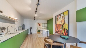 Uma cozinha moderna com armários verdes, uma área de refeições com uma mesa redonda e um quadro grande na parede.