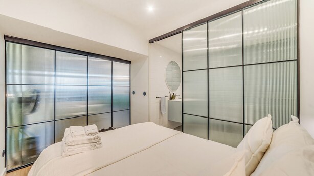 Quarto moderno com uma cama grande, uma porta de correr de vidro e um espelho na parede.