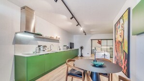 Uma cozinha moderna com armários verdes, coifa de aço inoxidável e um espaço de jantar com mesa redonda e cadeiras de madeira.