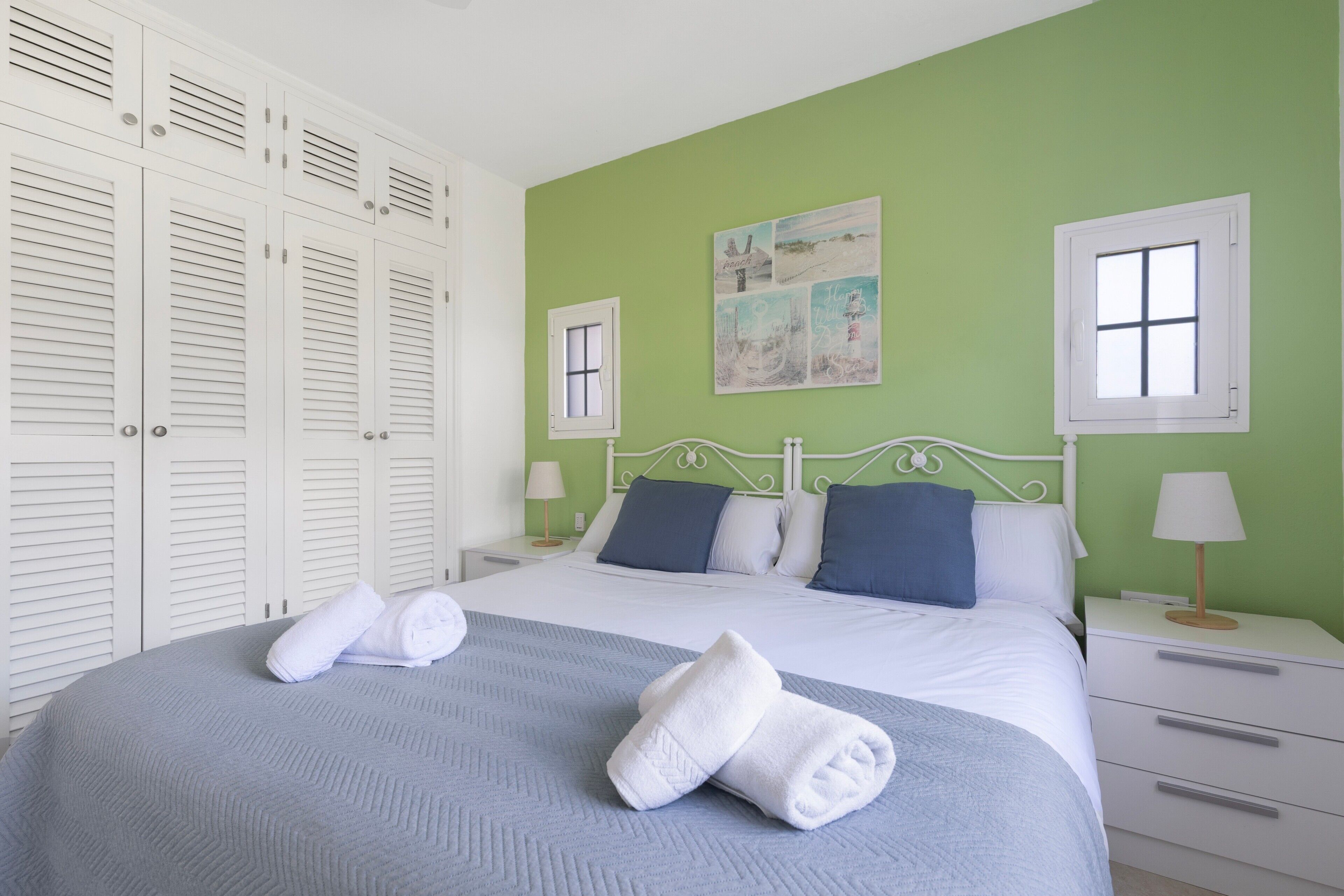 A neatly made bed with pillows, a bedside table with a lamp, and a wardrobe with louvered doors.