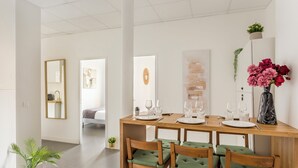A dining area with a wooden table set for four, green cushioned chairs, and a vase of flowers on the right. - Family Suite - Marais Turbigo I (Paris)