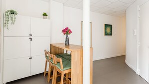A modern, minimalist room with a wooden dining table and chairs, a vase with pink flowers, and a green plant on a white cabinet. - Family Suite - Marais Turbigo I (Paris)