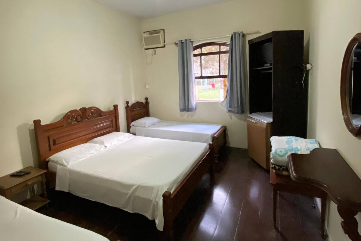 A bedroom with two single beds, a wooden wardrobe, a desk, a chair, a ceiling fan, and a window with curtains.
