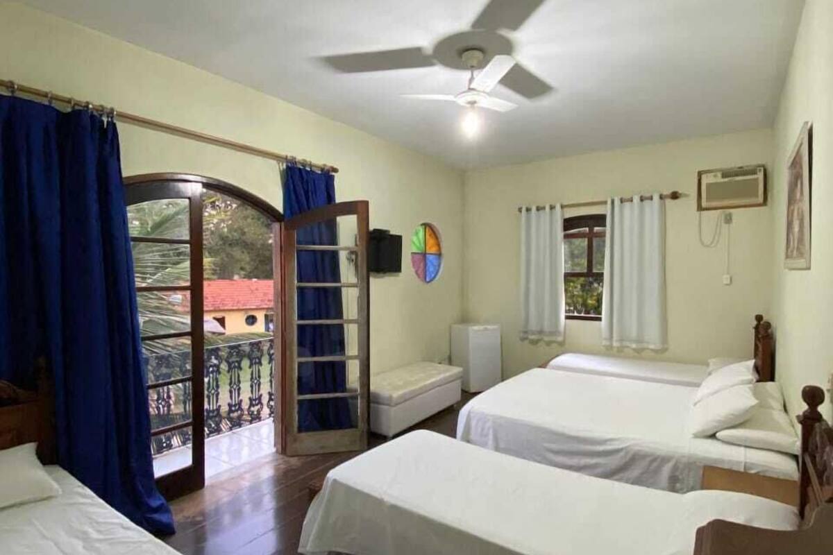 A hotel room with two beds, a ceiling fan, a small table, and a window with curtains.