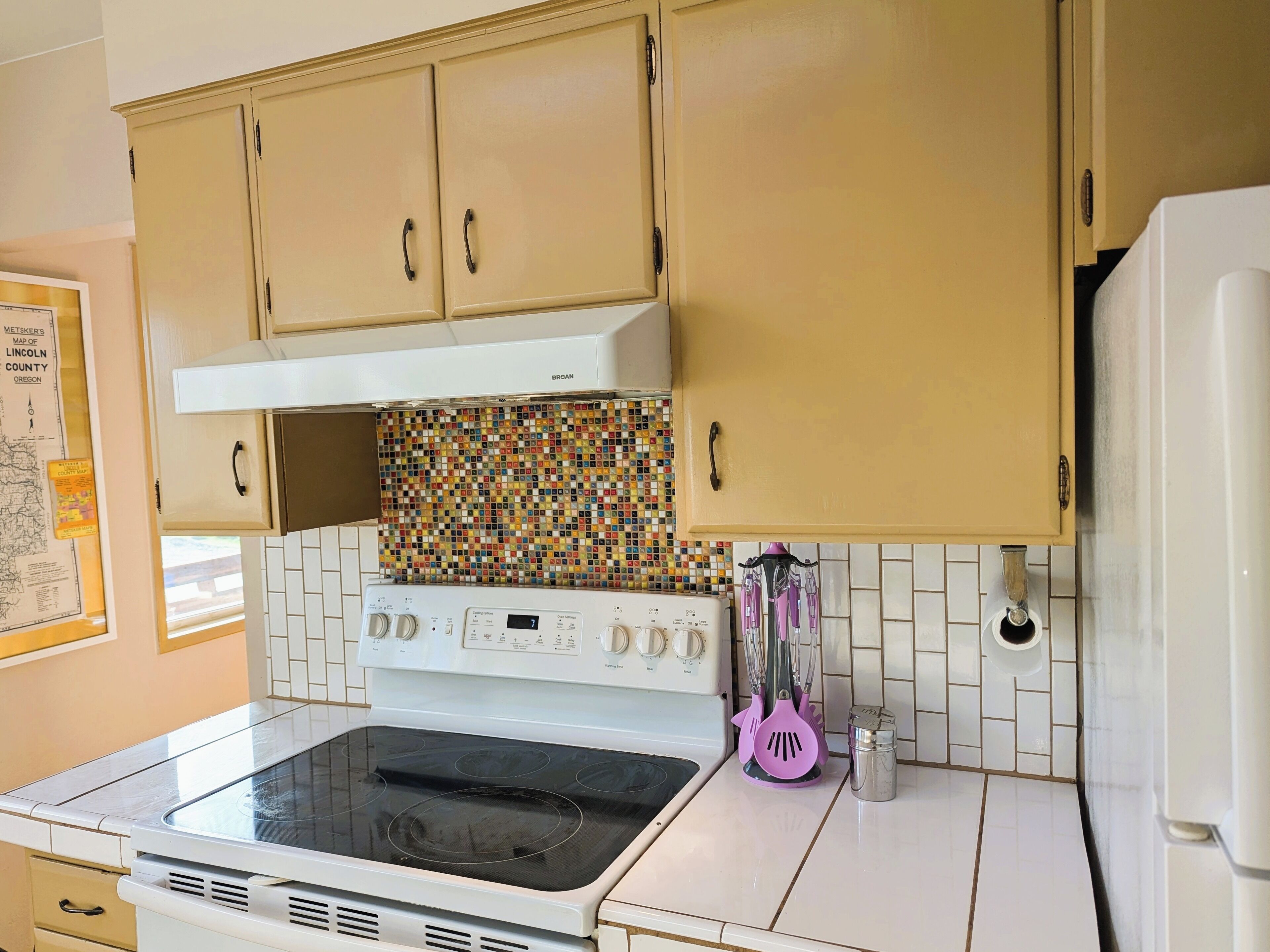 Une cuisine avec des meubles de couleur beige, une cuisinière blanche et un crédence colorée.