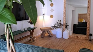 A living room with a green sofa, a wooden coffee table, a small wooden stool, and a large mirror. There is a potted plant in the foreground. - Logradouro House (Alcochete)