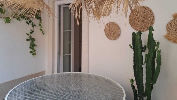 A room with a round glass table, a hanging woven light fixture, and a cactus plant. - Logradouro House (Alcochete)