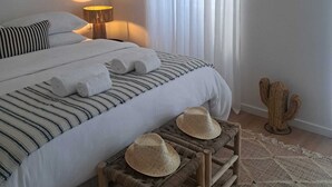 A bedroom with a bed, pillows, a bedside lamp, a window with curtains, and a wall-mounted decoration. - Logradouro House (Alcochete)