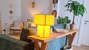 A modern living room with a wooden coffee table, a yellow lamp, a green sofa, and a potted plant. - Logradouro House (Alcochete)