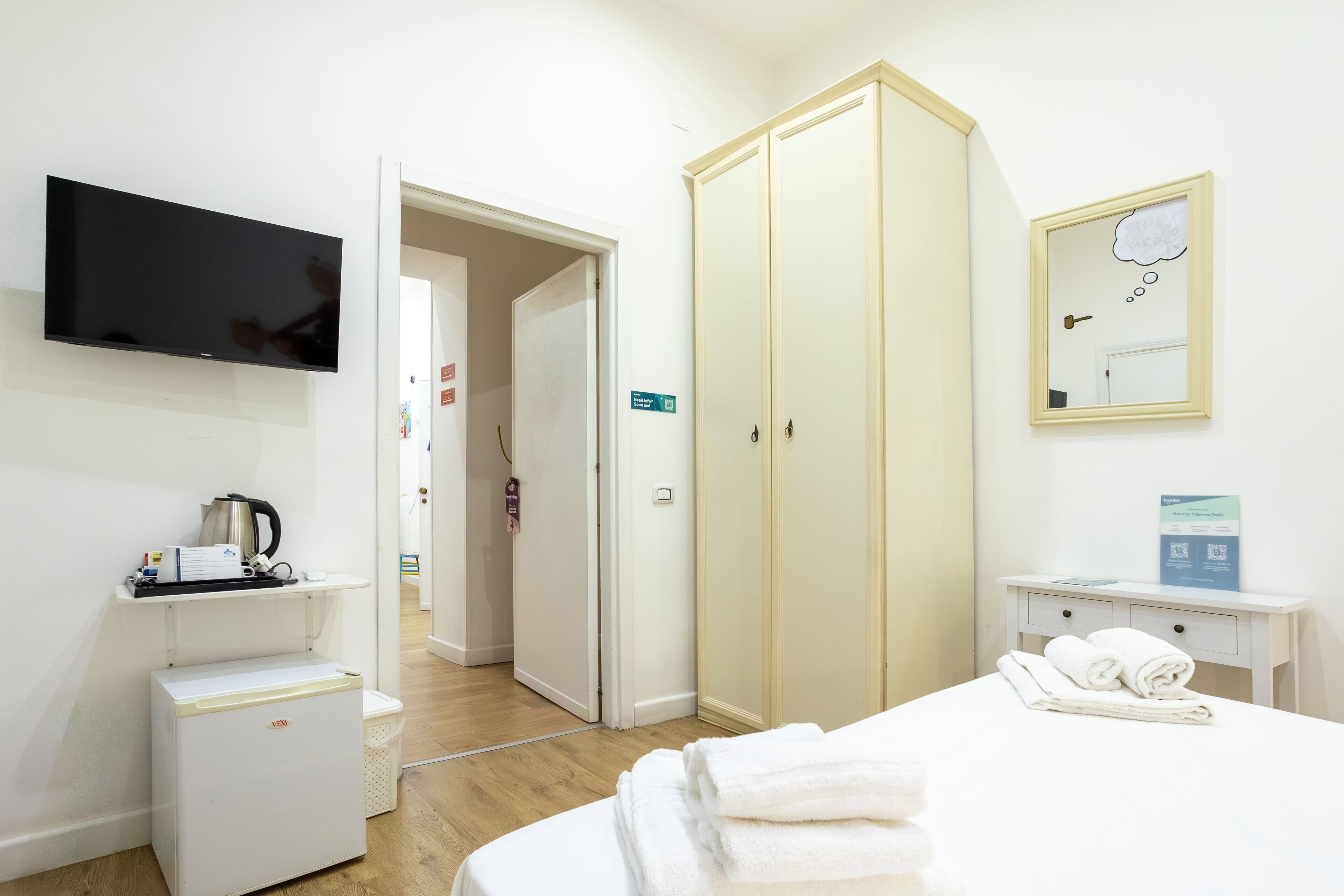 Ein Hotelzimmer mit Bett, Fernseher, Kleiderschrank, kleinem Tisch mit Wasserkocher und Mülleimer.