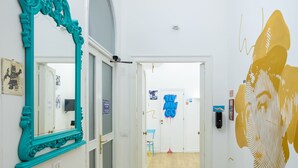 A hallway with a wooden floor, a teal-framed mirror, and a large gold mural on the wall. - Hotiday Palermo Porto (Palermo)