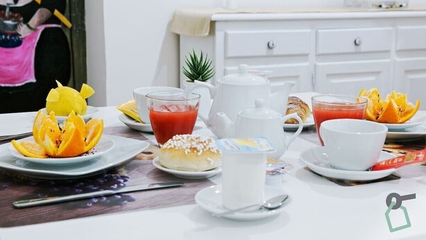 A breakfast setting with a table set for two, including plates with fruit, a teapot, cups, and a small plant on the side. - Hotiday Palermo Porto (Palermo)