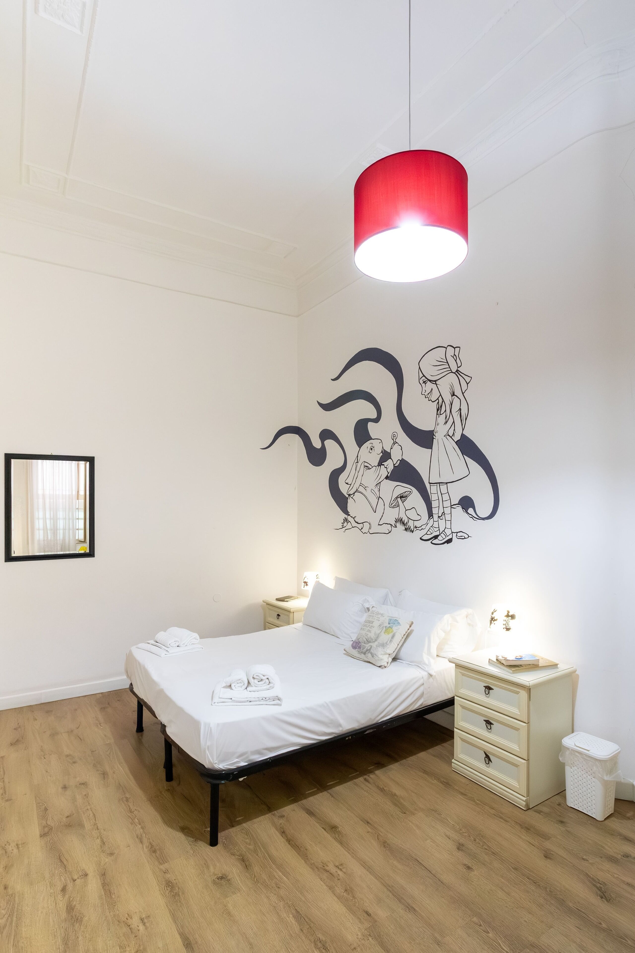 Une chambre à coucher comprenant un lit, des tables de chevet, une fresque murale et un luminaire rouge suspendu.