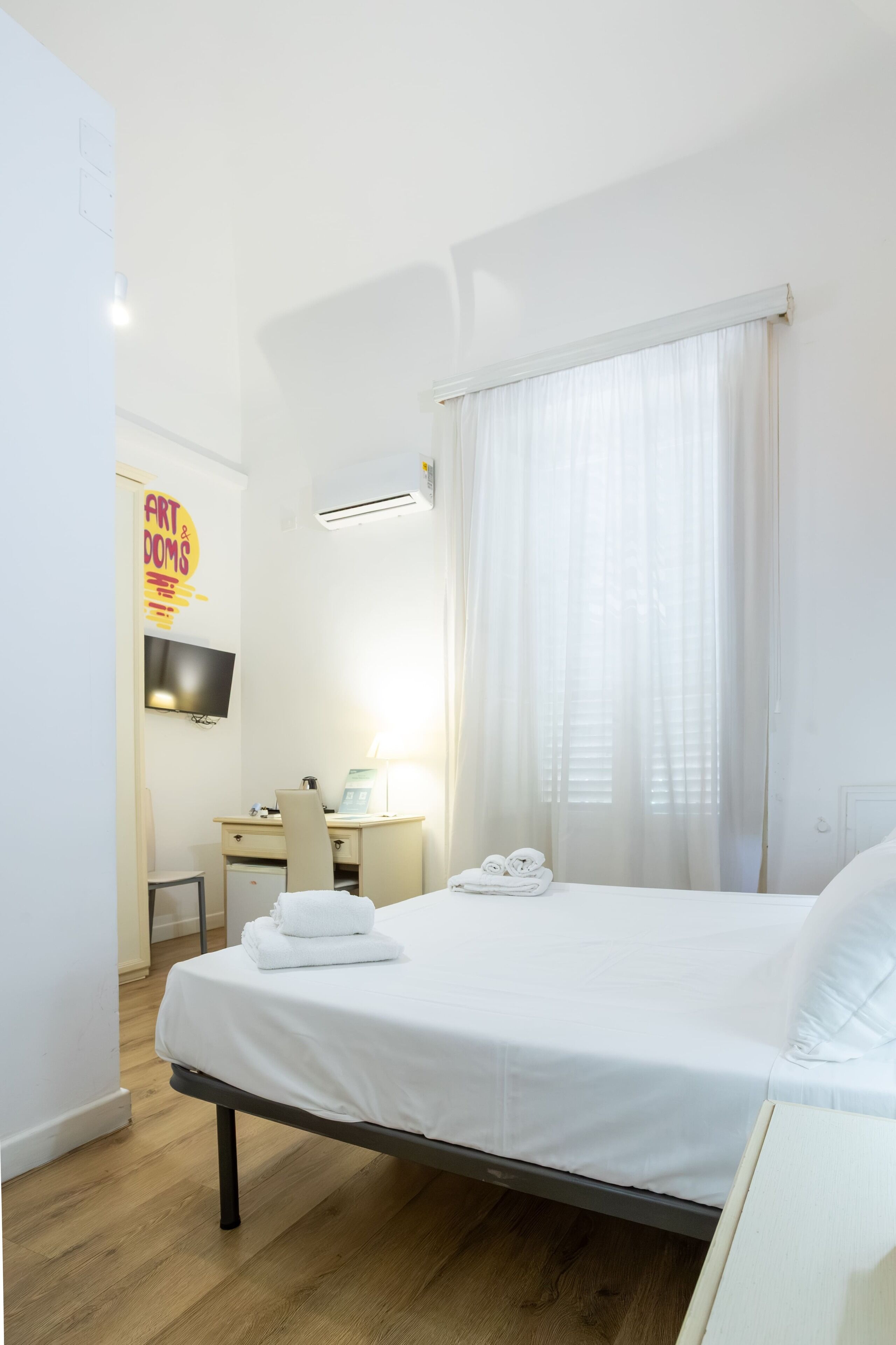 Una habitación de hotel con cama, escritorio, silla, televisor y ventana con cortinas.