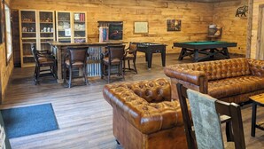 Ein gemütlicher Innenraum mit Billardtisch, Kicker, Ledersofa und einer Bar mit Sitzgelegenheiten.