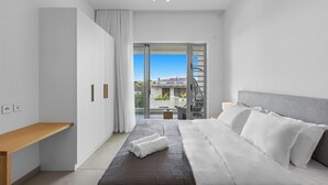 Habitación de hotel moderna con una cama grande, un banco de madera y un balcón con vista a la ciudad.