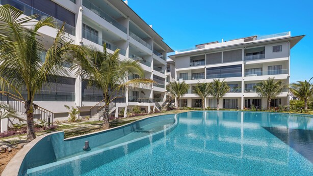 Un hotel moderno con una amplia piscina, varios balcones y palmeras.