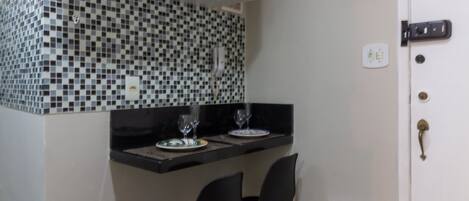 Cocina compacta con encimera negra, dos sillas negras y una puerta blanca.