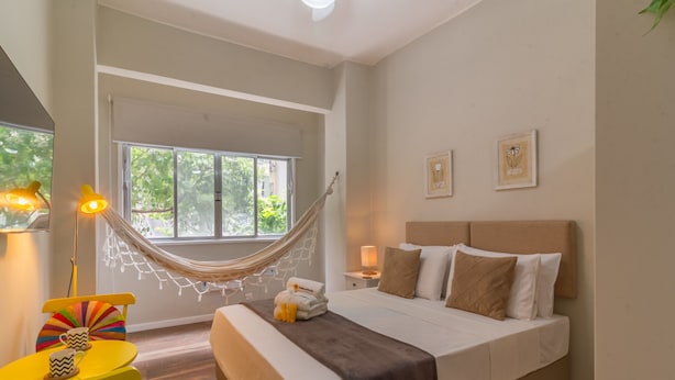 A bedroom with a bed, bedside table, lamp, chair, and a hammock. - 3 Minutes From Copacabana Beach Nsc220 (Rio de Janeiro)