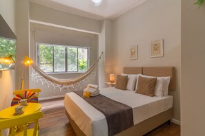 Un dormitorio con cama, mesita de noche, lámpara, silla y una hamaca.