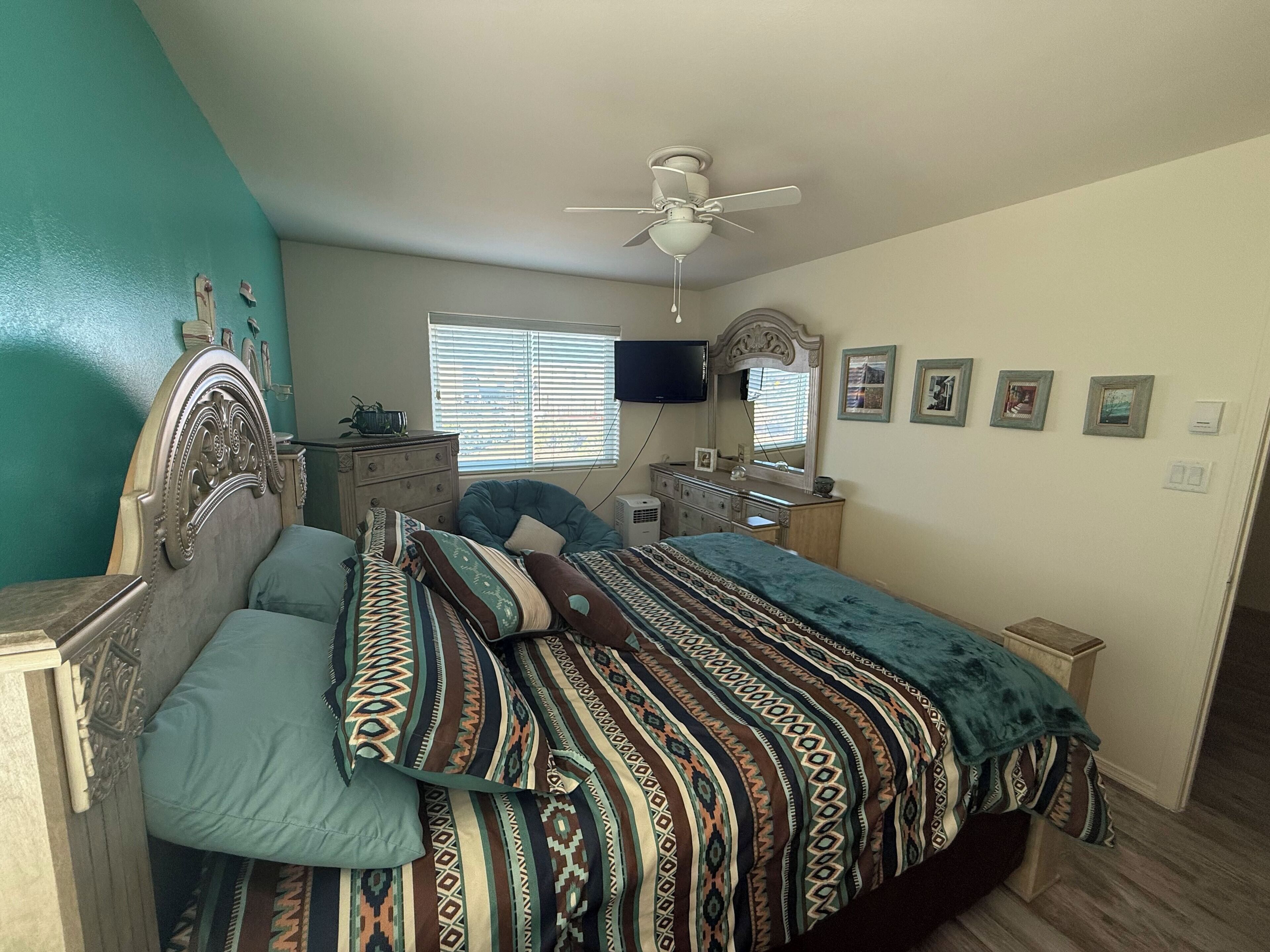 Une chambre à coucher comprenant un lit, une commode, une coiffeuse et un ventilateur de plafond.