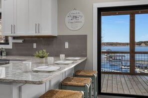 Una cocina con armarios blancos, encimera de mármol y vistas a un lago a través de un ventanal.