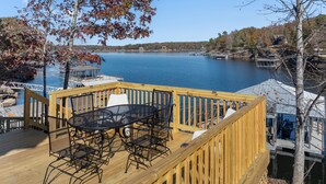 A wooden deck with outdoor seating overlooking a lake, docked boats, and a pier.