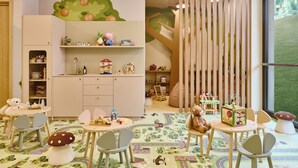 Un cuarto de juegos infantil con un ventanal amplio, una mesa de juegos y diversos juguetes y material educativo.