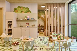 A children's playroom with a large window, a play table, and various toys and educational items. - Falkensteiner Resort Lake Garda (Salò)