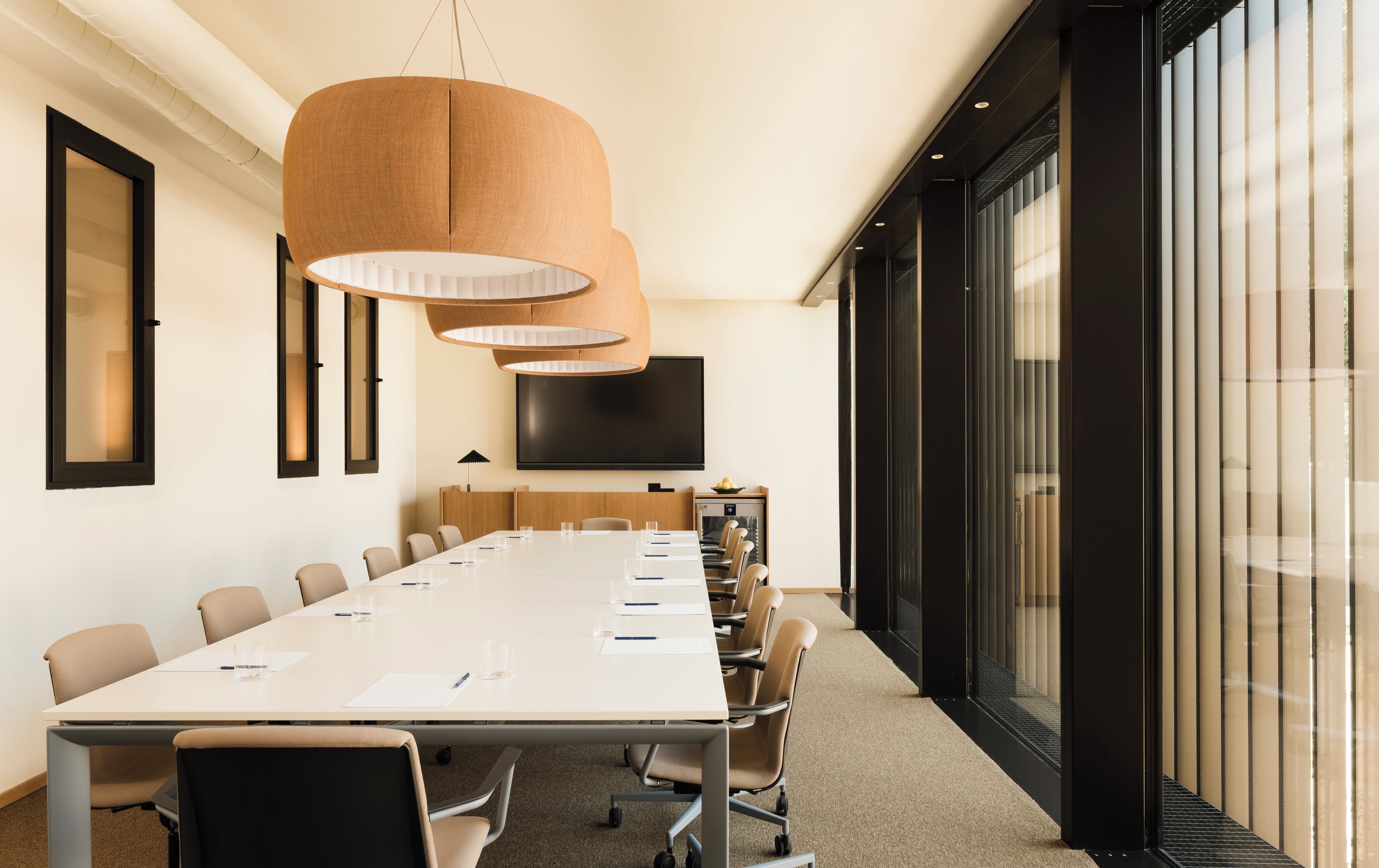 A conference room with a long table, chairs, a large screen, and a modern pendant light.
