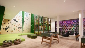 A climbing wall, a foosball table, and a sofa in a modern indoor space.