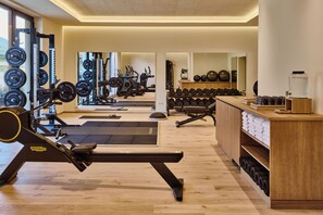 A modern gym with various exercise equipment, including a rowing machine, dumbbells, and weight plates. - Falkensteiner Resort Lake Garda (Salò)